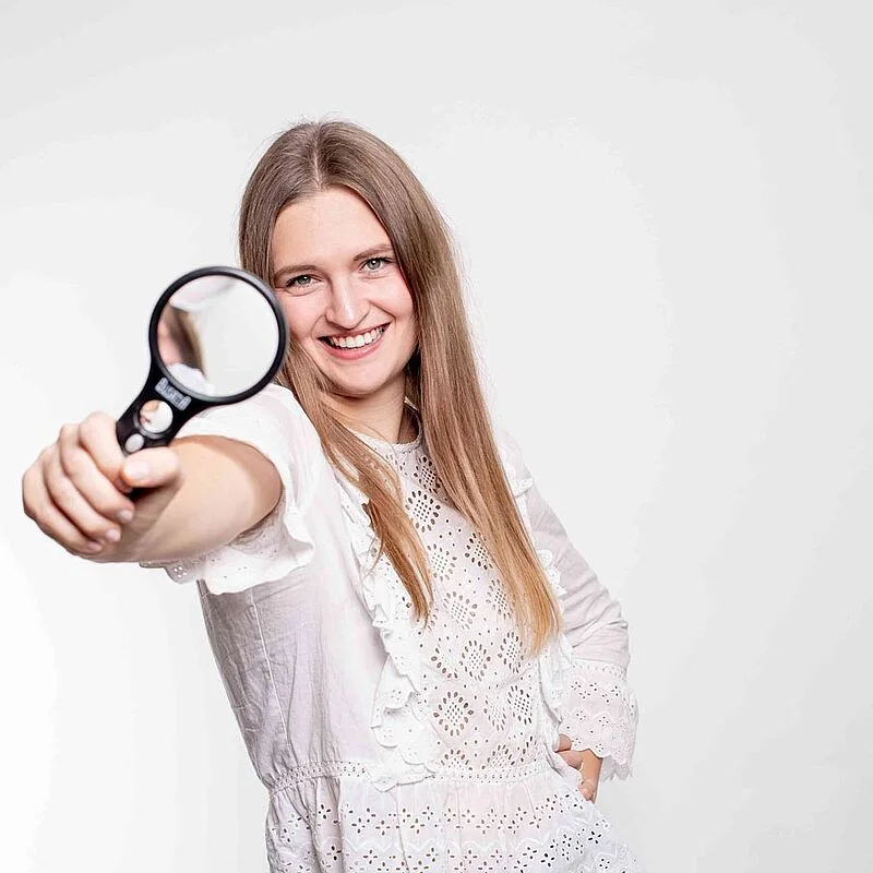 Beamtin schaut sich Dienstunfähigkeitsversicherung mit Lupe genau an | OPTINVEST